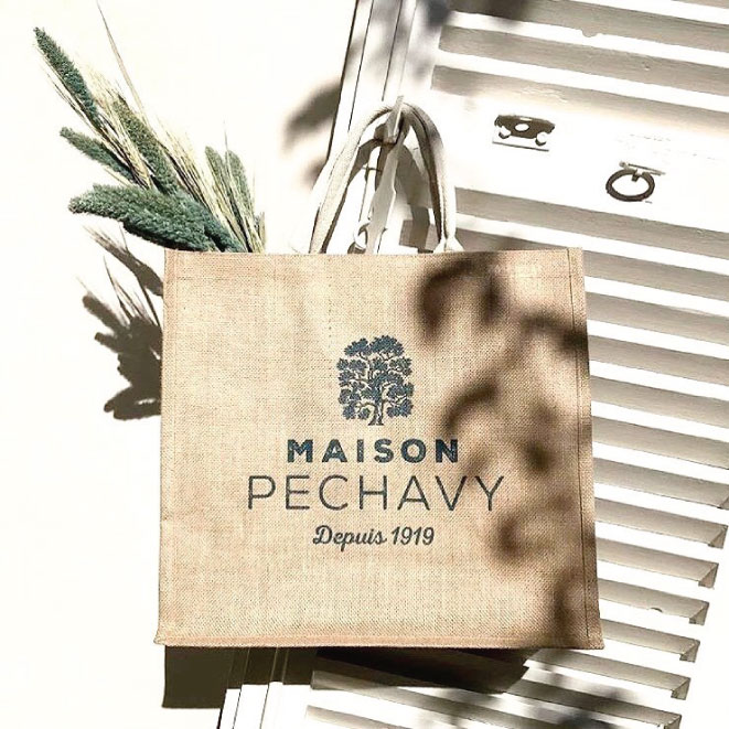 A stack of large, eco-friendly wholesale hessian tote bags screen-printed with a corporate logo in blue ink.